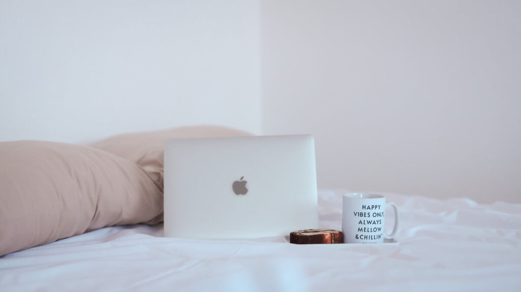 「ベッドに置かれたパソコンとマグカップとお菓子」のイメージ画像